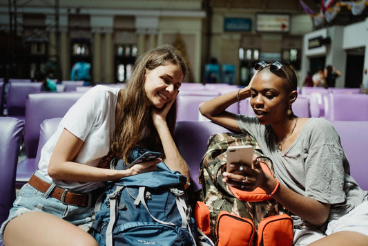 Two backpackers looking at a phone while seated in a train terminal